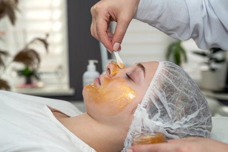 Young caucasian in spa getting anti-aging cosmetic treatment with golden mask on face. Deep moisturizingの写真素材