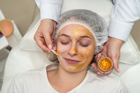 cosmetologist applying gold facial mask by brush on face female client at spa. Healthcare conceptの写真素材