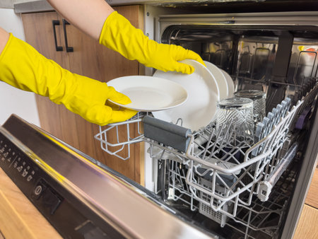 close up woman in yellow gloves loading dishes in dishwasher machine. Kitchen appliances, lifestyleの写真素材