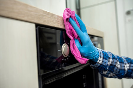 Cleaning lady's hands with a rag wiping the stove top and hood from greasy grease in the kitchen....