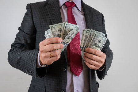 Man in suit holding and counting cash us dollar isolated on gray. Finance conceptの写真素材