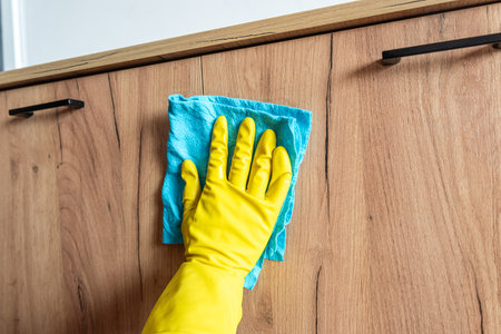 woman with yellow gloves wipes wooden table surface. Housekeeping