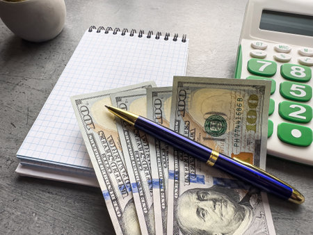 Empty notepad with us dollar currency pen and calculator on drey desk. Top view with copy space, business conceptの写真素材