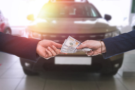 man gives dollar cash to dealer man when buying a car at modern showroom. Deal of buy or rent new autoの写真素材