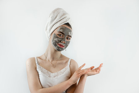 Portrait of pretty young woman wears beauty black clay mask on face isolated on white. Perfect skin concept, enjoys facial treatmentsの写真素材