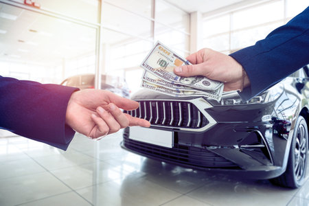 A successful purchase, the buyer gives dollars to the seller in a modern car dealership. Buying or...