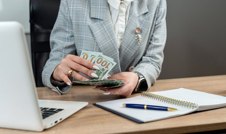 Paper dollar bills in the female hands and laptop empty notepad at office desk. Finance conceptの写真素材