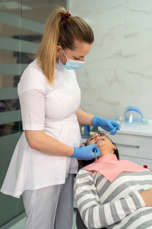 Dentist use dental tools for oral check up and examining cavities and gum at her female client at clinic. Concept of  conducting examination, treating teeth.の写真素材