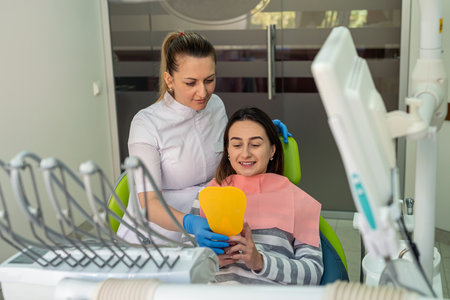 Feamle patient and a doctor are looking at the mirror and discussing the treatment of caries or gum disease. The client smiles. Oral enamel caries treatment.の写真素材