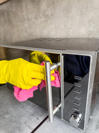 Closeup female hands wearing yellow rubber gloves with rag cleaning service wipe wooden countertop...
