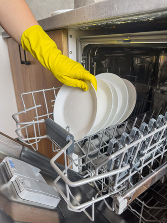 close up woman in yellow gloves loading dishes in dishwasher machine. Kitchen appliances, lifestyleの写真素材