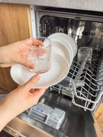 woman takes clean plates cups out of the dishwasher machine, household applianceの写真素材