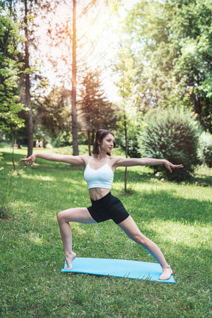 Slim pretty woman practicing relax yoga or pilates at nature. Time for sport at summer morning in the parkの写真素材