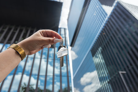 Real estate agent with house key against  background of skyscrapers in city. Sale or rent conceptの写真素材