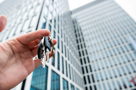 male real estate agent showing keys of new home house apartament against new modern glass building