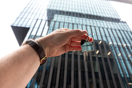 close up male agent show house key against modern office building, outsideの写真素材