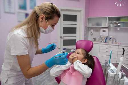 cute little girl is sitting on the dental chair and does not want to treat her teeth by showing appropriate gestures. concept of fear of dentists. healthy oral cavityの写真素材