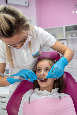 Close-up of a beautiful little girl opening her mouth wide during dental treatment at a woman's dentist. treatment of children's teeth. dentistryの写真素材