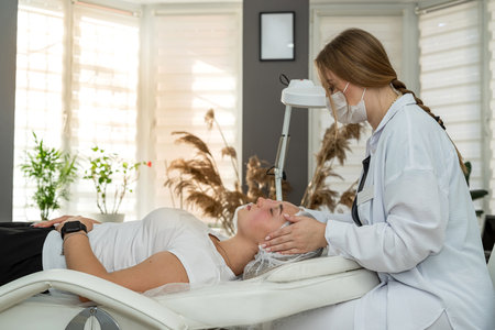 beautician doing relaxing facial massage to young caucasian woman at spa salon. Concept of rejuvenation procedureの写真素材