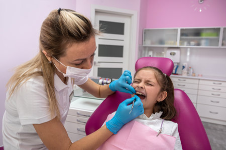 beautiful little female patient grimaces during an examination of the oral cavity by a female dentist. toothache in children. oral healthの写真素材