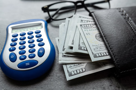 Business concept with calculator, glasses, us dollar money on black male wallet on grey deskの写真素材