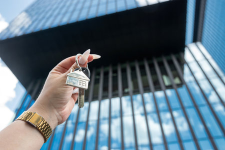 Real estate agent with house key against background of skyscrapers in city. Sale or rent conceptの写真素材