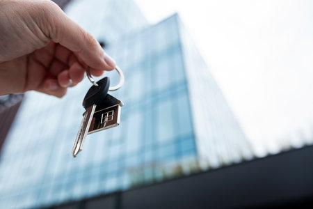 close up male agent show house key against modern office building, outsideの写真素材