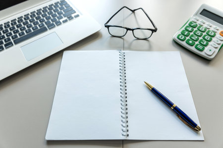 White office desk with laptop blank notepad calculator and pen eyeglasses. Workplaceの写真素材