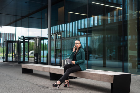 pretty caucasian businesswoman is walking and talking by phone near modern office building aの写真素材
