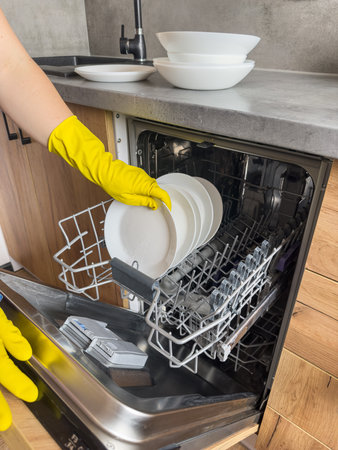 Woman in gloves placing plate and glasses in automatic built-in dishwashers machine. Household domestic lifeの写真素材