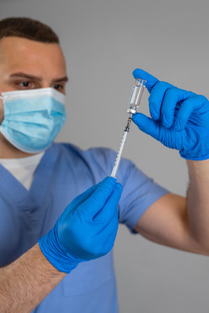Professional caucasian doctor holding a syringe with vaccine isolated on grey. Healthcare and medicineの写真素材