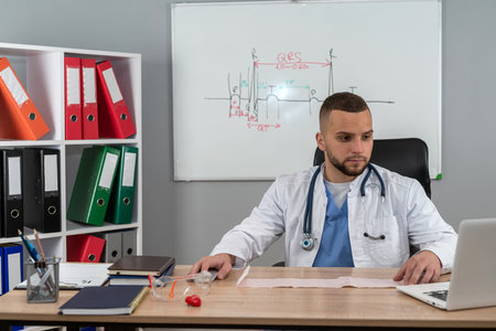 Portrait of man doctor therapist practitioner in white coat and stethoscope working at desk alone in modern clinic. Distance medicine conceptの写真素材