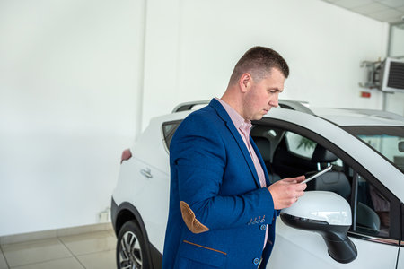 Satisfied happy young male customer choosing new car at showroom or dealership. vehicle sale conceptの写真素材