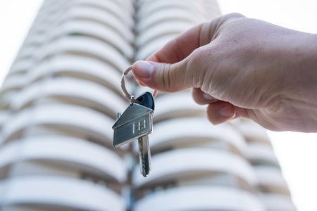 female real estate worker hold keys to apartment on background of multi-storey building. Purchase conceptの写真素材