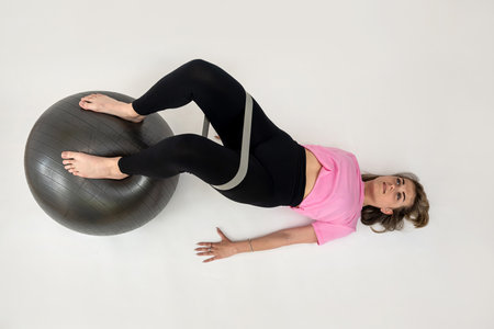 Slim caucasian woman make exercises using rubber bands and fitness ball isolated on white. Home workoutの写真素材