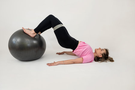 sporty attractive woman doing stretching exercising with fit ball and rubber band isolated on white. Works on musclesの写真素材