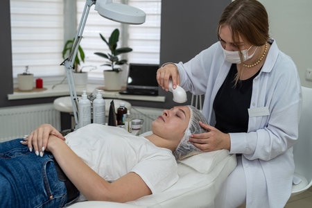 beautician doing cosmetic procedures ultrasonic cavitation facial peeling her female caucasian client. Cosmetology and face skin careの写真素材