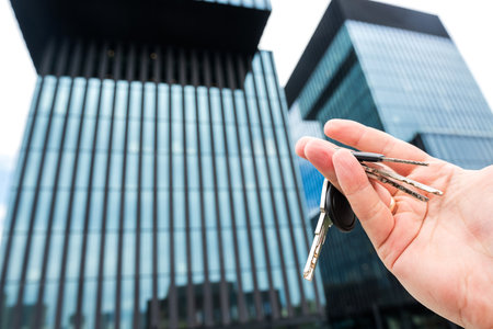 House keys in real estate agent against new skyscraper glass office. Concept of moving home or renting propertyの写真素材
