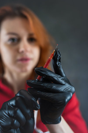 female doctor wearing red uniform medical gloves holding a syringe with blood isolatedon black. Healthy lifestyleの写真素材