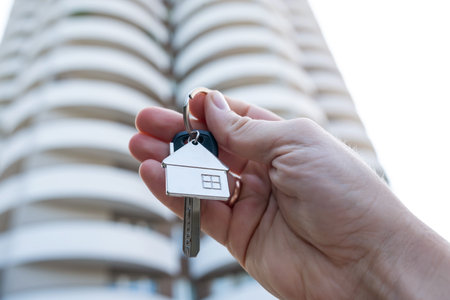 woman real estate agent holding house key on background of new buildings. Purchase conceptの写真素材