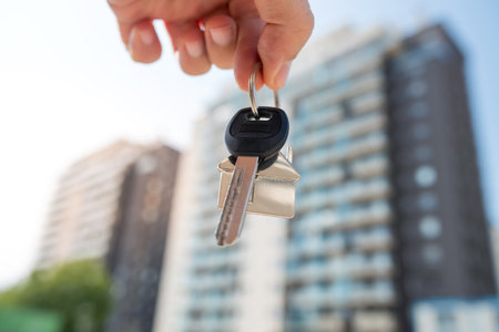woman real estate agent holding house key on background of new buildings. Purchase conceptの写真素材