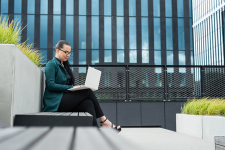 Businesswoman work on notebook or laptop computer at outdoor modern glass building cityscape in the backgroundの写真素材