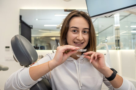 Portrait of beautiful girl patient holding orthodontic retainers aligners in dental clinic. healthy straight teeth.の写真素材