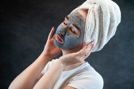 young beautiful woman wear white towel doing beauty wellness treatment with black clay facial mask. Anti aging treatment, skincareの写真素材