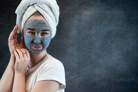 Woman in white towel with black charcoal face mask isolated on black. Skincare concept, anti aging treatment. Cosmetic procedures, beauty wellness treatment at homeの写真素材