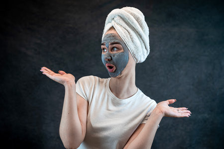 Woman in white towel with black charcoal face mask isolated on black. Skincare concept, anti aging treatment. Cosmetic procedures, beauty wellness treatment at homeの写真素材