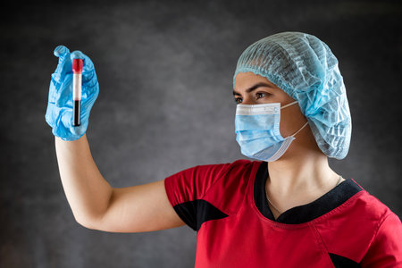 Female nurse or doctor wear red uniform holding blood test result coronavirus COVID-19 isolated on black. Medical researchの写真素材