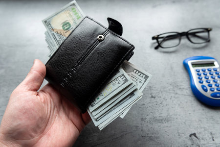 male hand hold full us dollar money black wallet on grey background. Financial concept