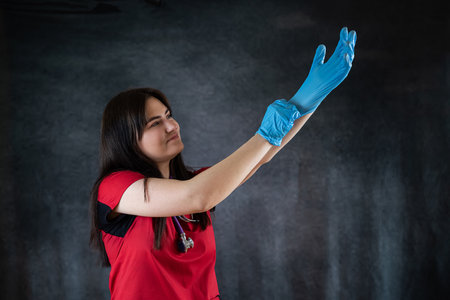 Female nurse wear red uniform putting on blue gloves. Medical healthcareの写真素材