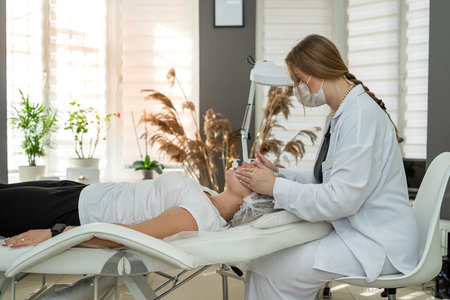 beautician applies the white moisturizing cream to female face patient at beauty studio. Healthy lifestyle anti wrinkle proceduresの写真素材